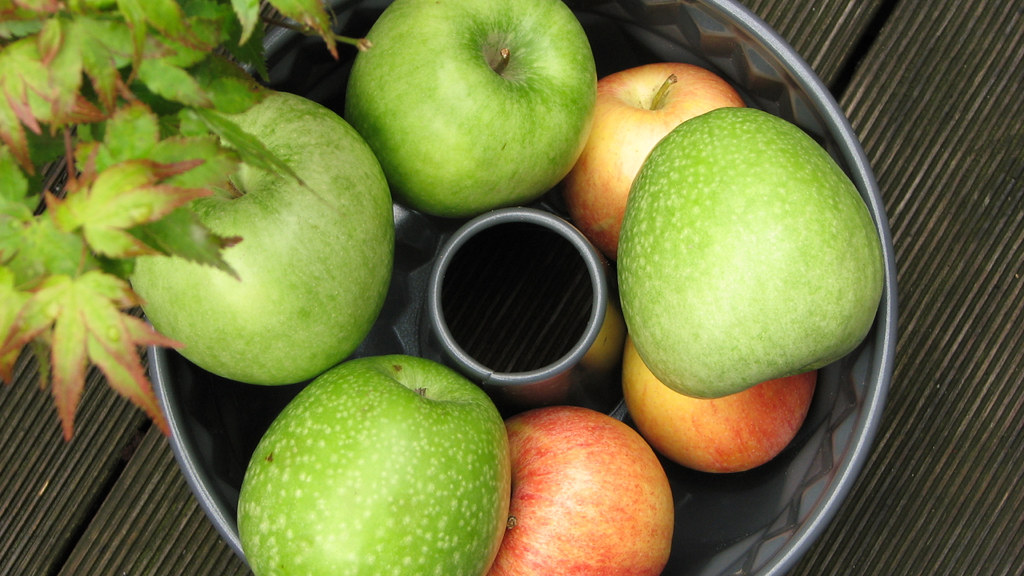 Several green and red apples in a bundt cake tin on a balcony under a Japanese maple