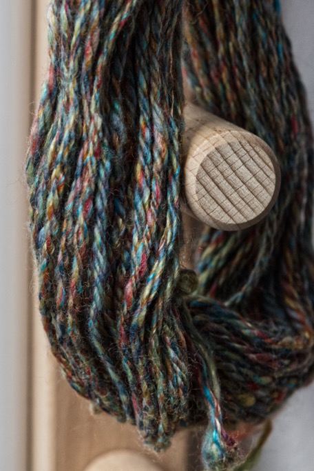 Chain plied handspun skein of multi-coloured wool hanging on a warping frame