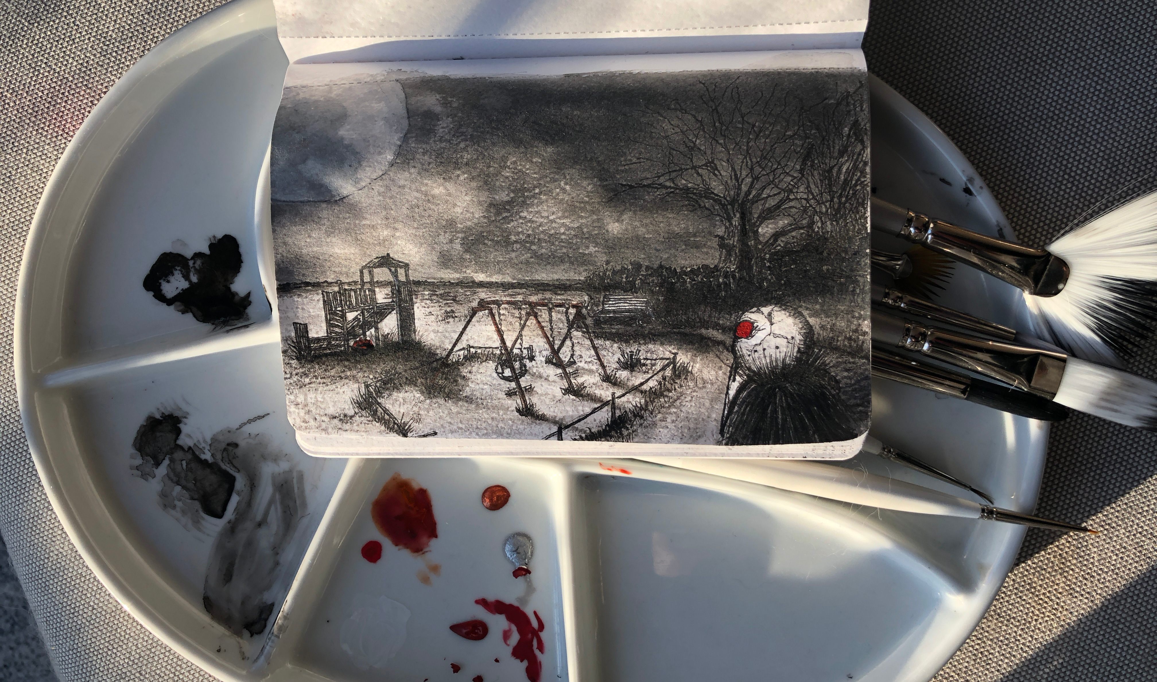 An Halloween ink painting in a small sketchbook resting on a porcelain palette