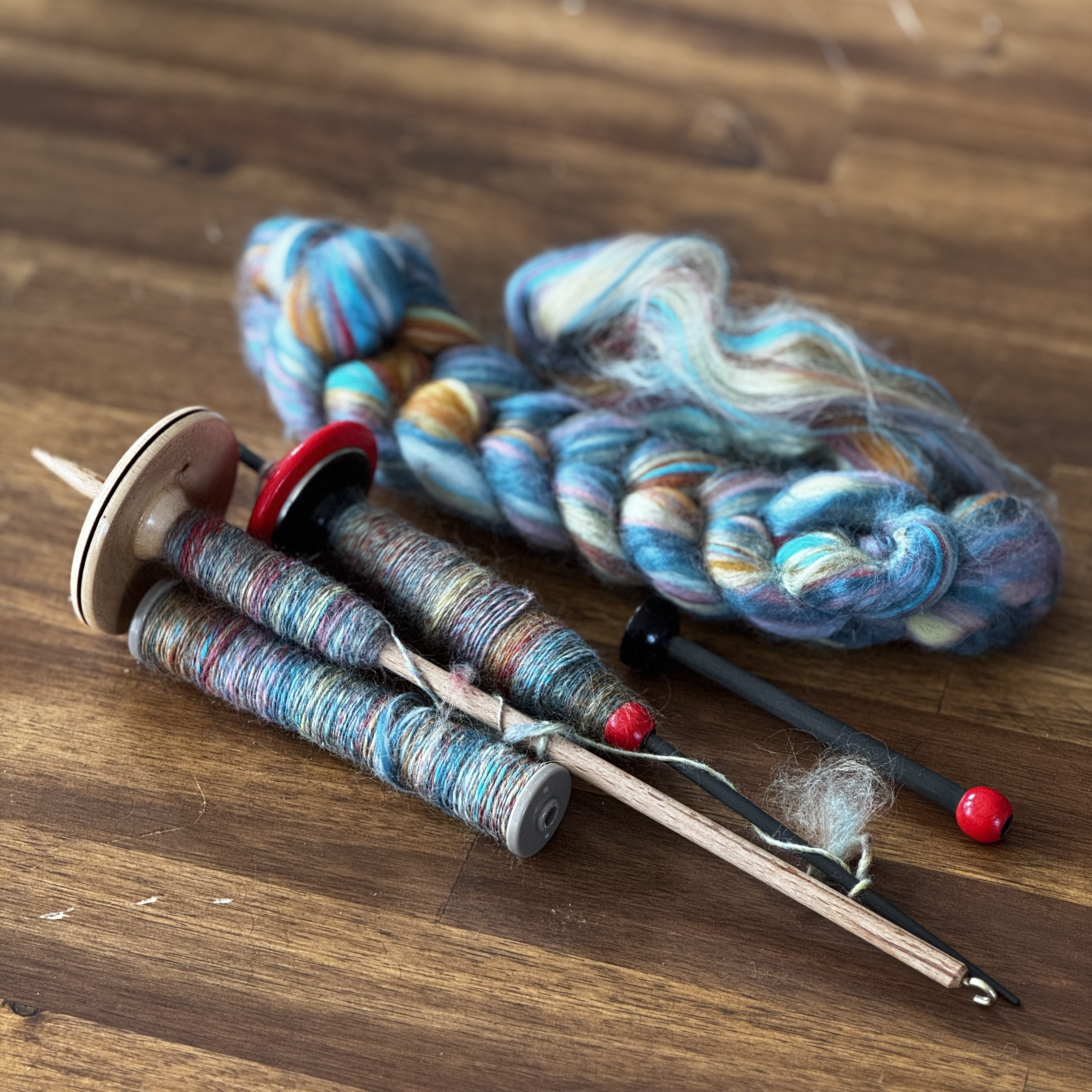 A hand holds a red and black carbon supported spindle with a removeable bobbin and a handspun multi-coloured yarn