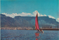 Blank postcard - Red sails rise up against Table Mountain as a yacht makes its way back to the Yacht Basin in the Duncan Dock. The tall building to the left of the yacht is the Sanlam Building, 297 ft. high, and one of the tallest buildings in Africa